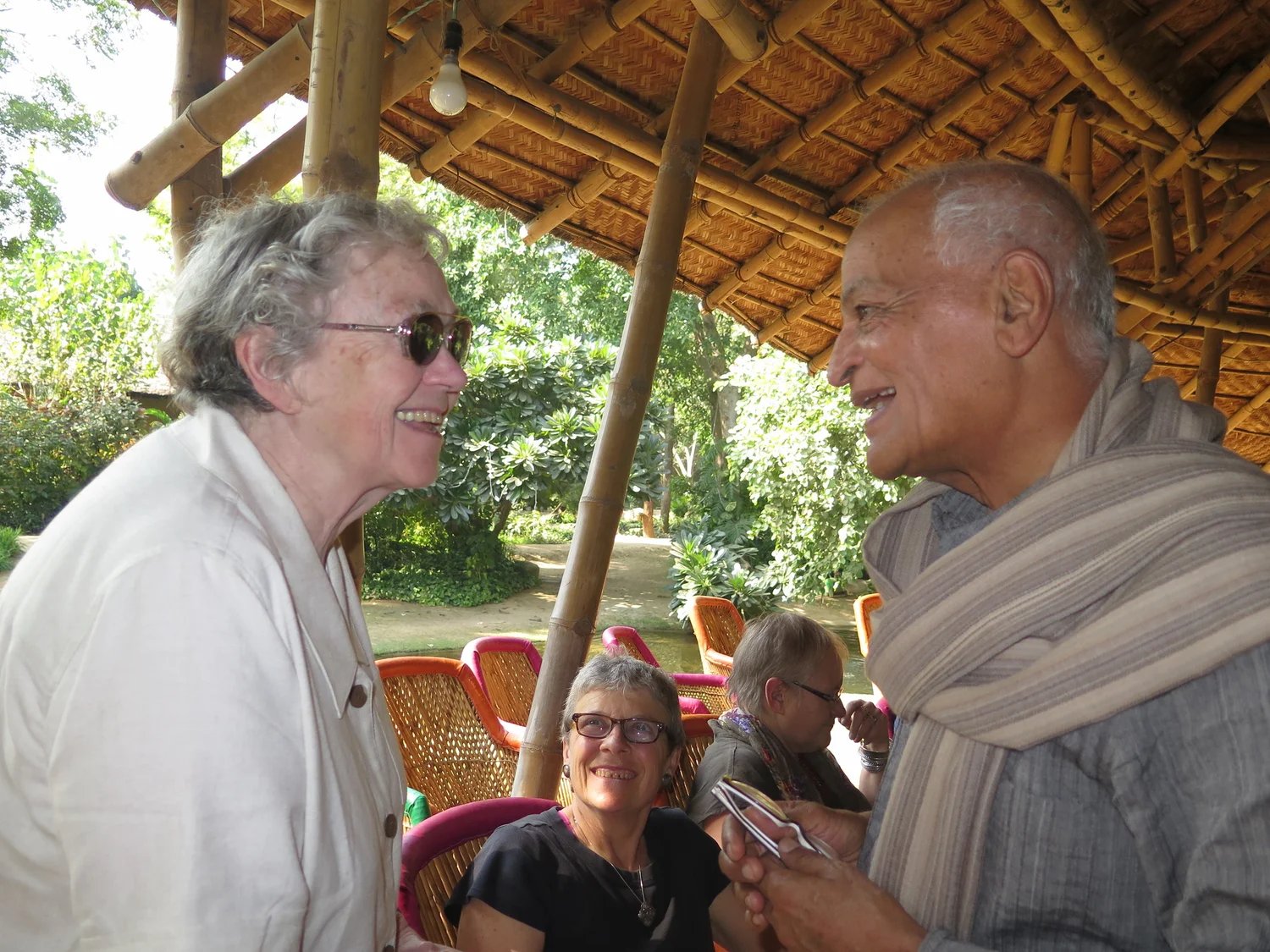 Two elders laughing together beneath a thatched roof